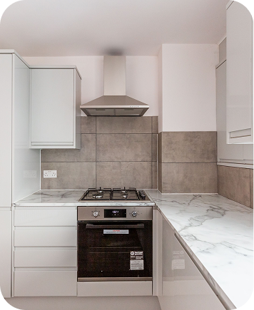 Modern kitchen with white cabinets, marble countertop, a built-in oven, and a gas stove under a stainless steel range hood. The backsplash features large gray tiles.