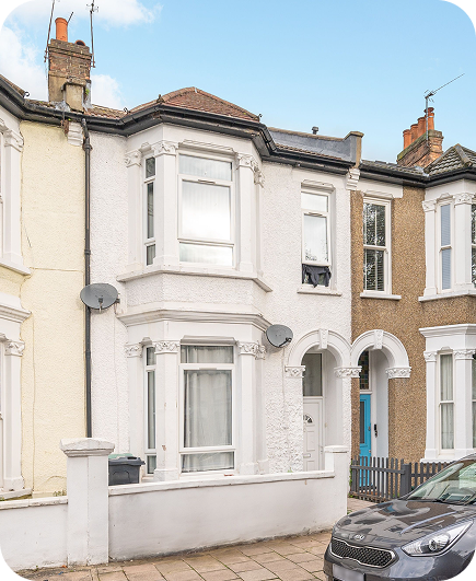 A white terraced house with bay windows, ornate details, two satellite dishes, and a small front yard, situated between yellow and brown neighboring houses. A gray car is parked in front.