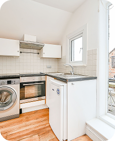 A compact, modern kitchen with a washing machine, oven, stove, small refrigerator, white cabinets, tiled backsplash, wood floor, and a window letting in natural light.