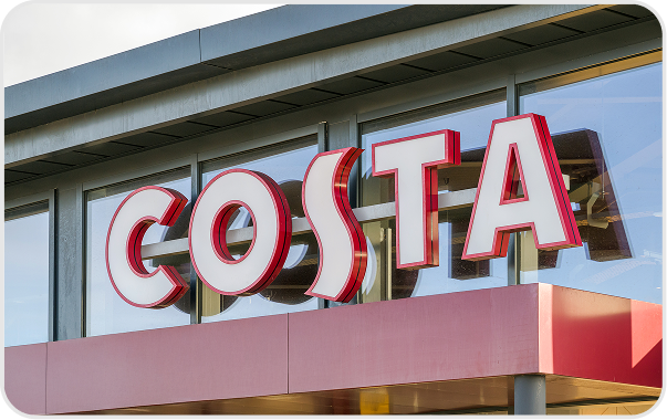 Exterior of a Costa coffee shop with large, bold red and white COSTA sign displayed on glass windows above the entrance.