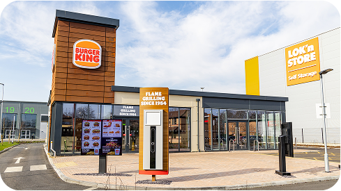 A modern Burger King restaurant with a drive-thru lane and menu board, next to a Lok’n Store self-storage building on a clear day.