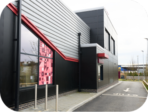 A modern fast-food restaurant with black and gray exterior panels, large windows featuring pink patterned decals, and a drive-thru lane running alongside the building.